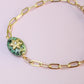 Gold bracelet with a greenstone bead on a light pink background