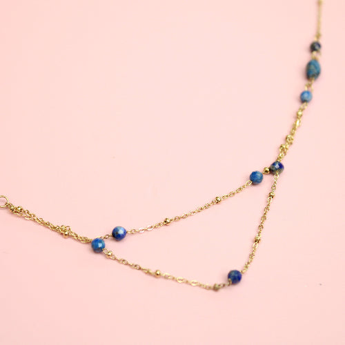 Gold necklace with blue beads on a pink background