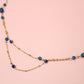 Gold necklace with blue beads on a pink background