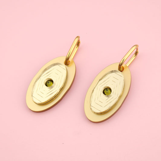 Gold earrings with green gemstones on a pink background