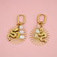 Gold earrings with sunburst design and opal stones on a pink background