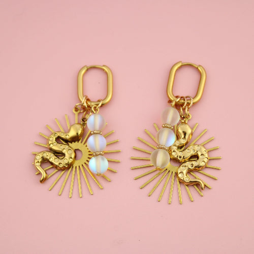 Gold earrings with sunburst design and opal stones on a pink background
