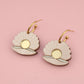 Pair of earrings with gold and beige design on a pink background