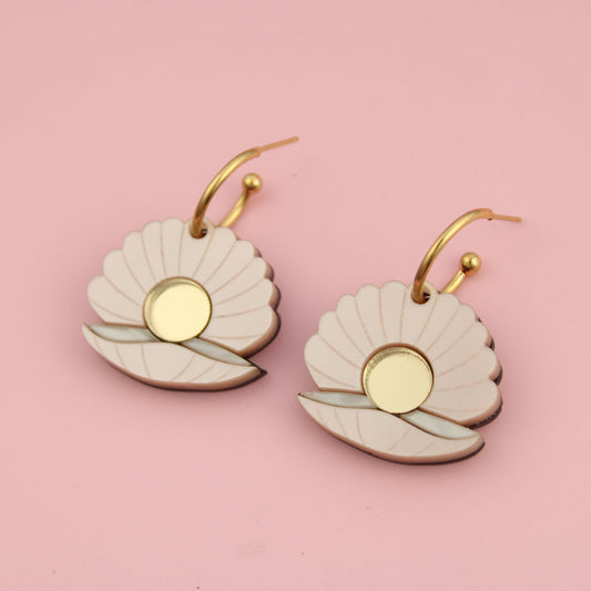 Pair of earrings with gold and beige design on a pink background
