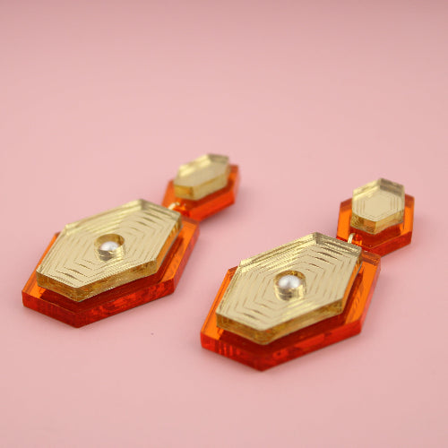 Pair of orange and gold earrings on a pink background