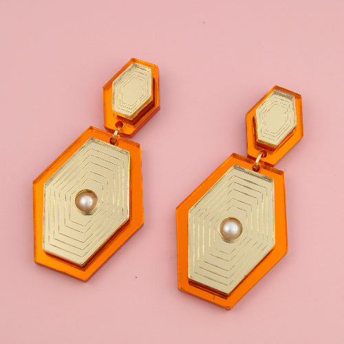 Hexagonal gold and orange earrings on a pink background