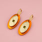 Pair of earrings with orange and gold design on a pink background
