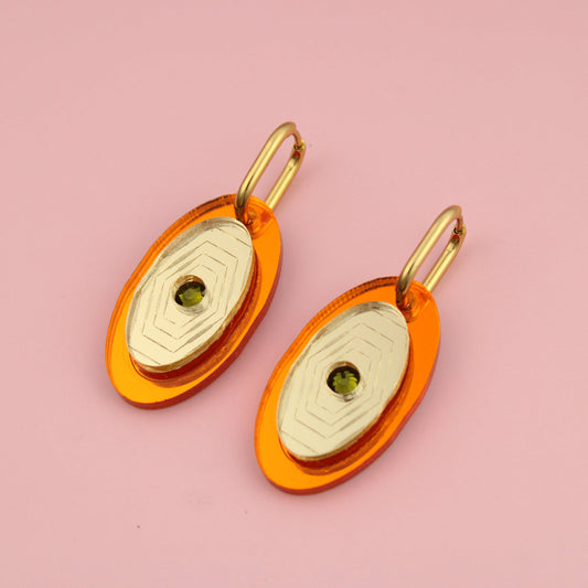 Pair of earrings with orange and gold design on a pink background