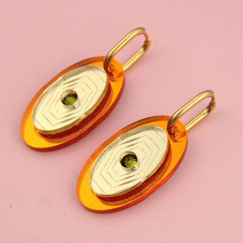 Gold and orange earrings on a pink background