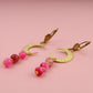 Gold earrings with pink beads on a pink background