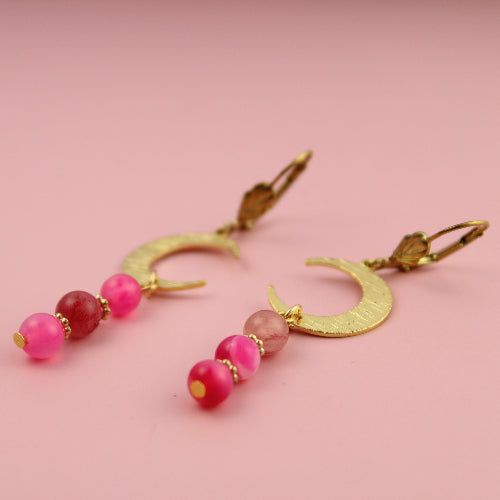 Gold earrings with pink beads on a pink background