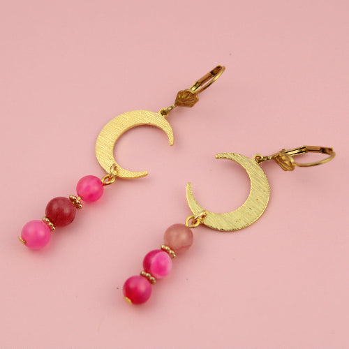 Gold crescent moon earrings with pink beads on a pink background