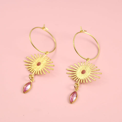 Gold hoop earrings with sunflower designs and pink gemstones on a pink background