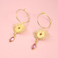 Gold earrings with sunburst designs and pink gemstones on a pink background