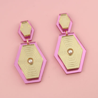 Hexagonal pink and gold earrings on a pink background