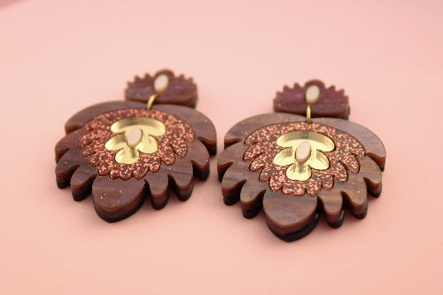 Pair of acrylic earrings with gold accents on a pink background