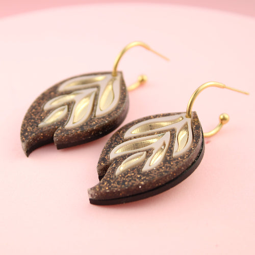 Pair of leaf-shaped earrings on a pink background