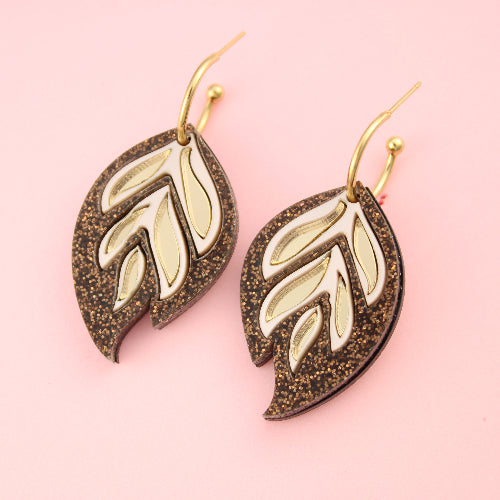 Leaf-shaped earrings with gold and bronze finish on a pink background