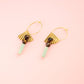 Gold earrings with green beads on a pink background