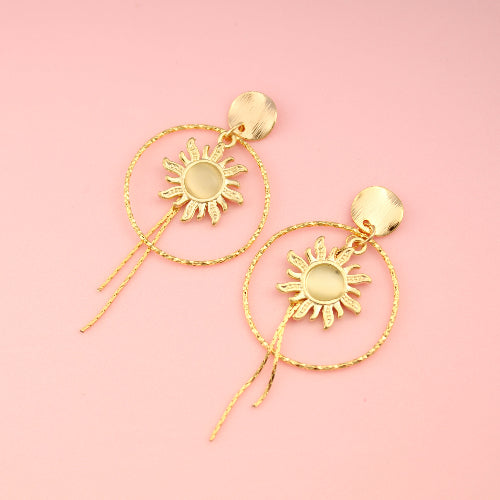 Gold sun-shaped earrings on a pink background