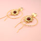 Gold earrings with sunflower design on a pink background