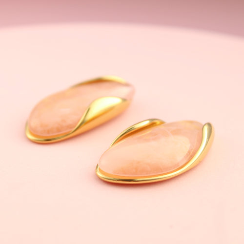 Pair of pink earrings with gold accents on a pink background