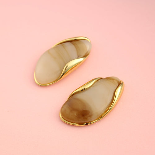 Pair of gold and beige earrings on a pink background