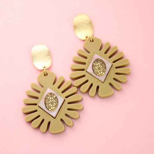 Gold earrings with a sunburst design on a pink background