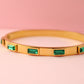 Gold bracelet with emerald green gemstones on a pink background