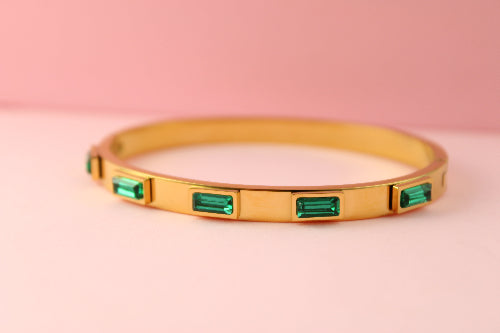 Gold bracelet with emerald green gemstones on a pink background