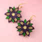 Floral earrings with purple, green, and gold colors on a pink background