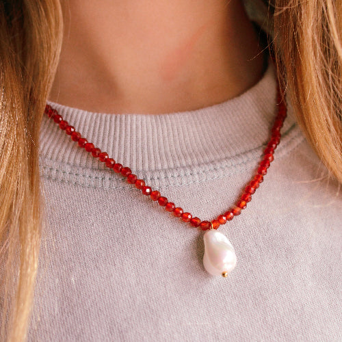 Close-up of a person wearing a red beaded necklace with a pearl pendant.