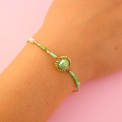 Green beaded bracelet on a wrist against a pink background