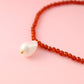 Necklace with red beads and a white pendant on a pink background