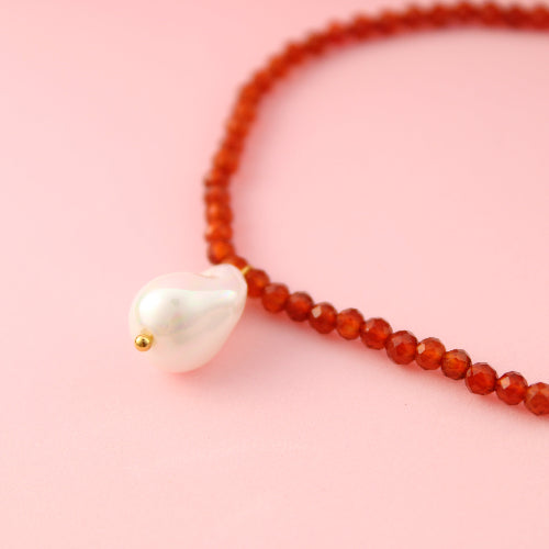 Necklace with red beads and a white pendant on a pink background