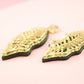Gold leaf-shaped earrings on a pink background