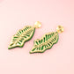 Green leaf-shaped earrings on a pink background