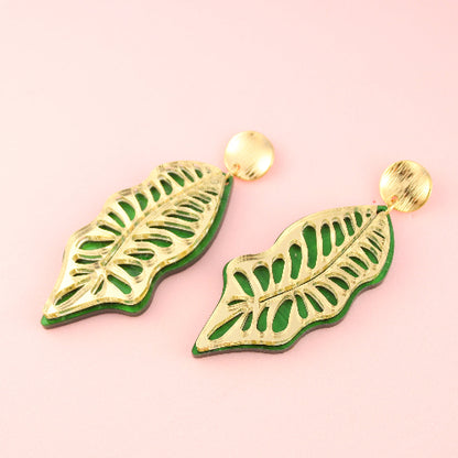 Green leaf-shaped earrings on a pink background