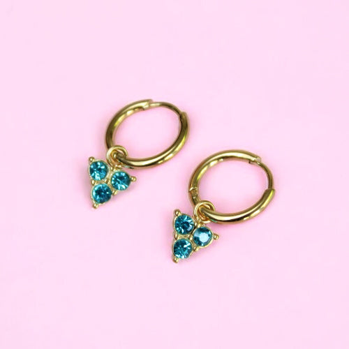 Gold hoop earrings with blue gemstones on a pink background