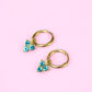 Gold hoop earrings with turquoise stones on a pink background