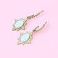 Pair of earrings with light blue stones and gold frames on a pink background