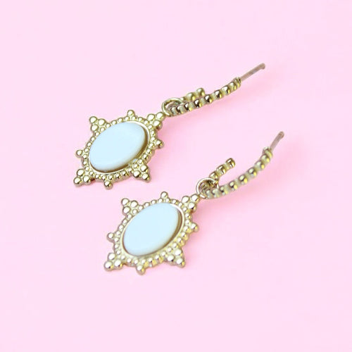 Pair of earrings with light blue stones and gold frames on a pink background