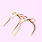 Gold bow-shaped earrings on a pink background