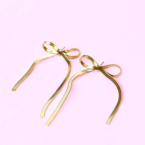 Gold bow-shaped earrings on a pink background