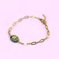 Gold bracelet with a green gemstone on a pink background