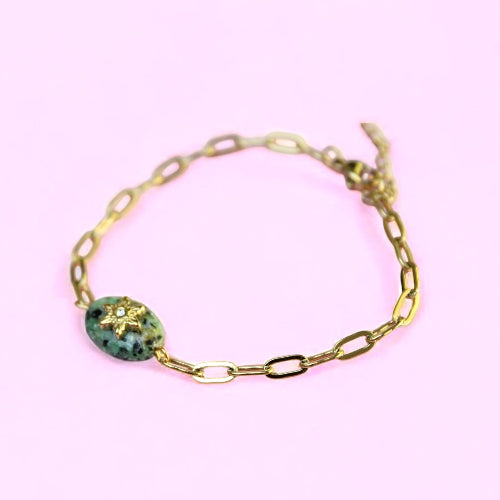Gold bracelet with a green gemstone on a pink background