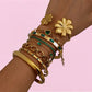 Gold and green gemstone bracelets on a wrist against a pink background