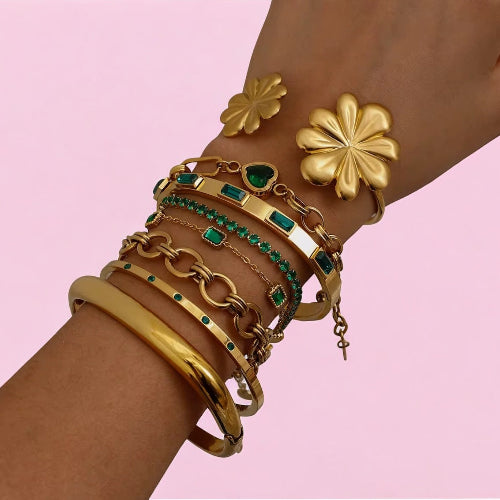 Gold and green gemstone bracelets on a wrist against a pink background