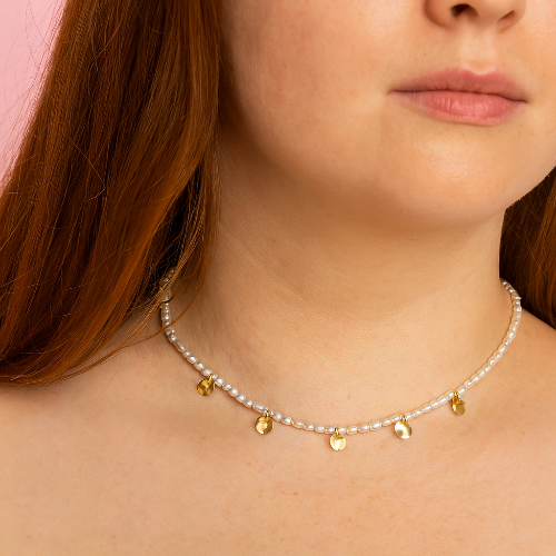 Close-up of a woman wearing a delicate necklace with small gold pendants against a pink background