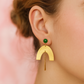 Gold earring with a green gemstone worn by a person against a pink background